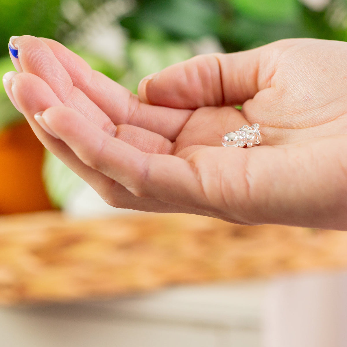 A silver cat charm with intricate detailing, displayed on a soft fabric background, by Scarlett Jewellery.