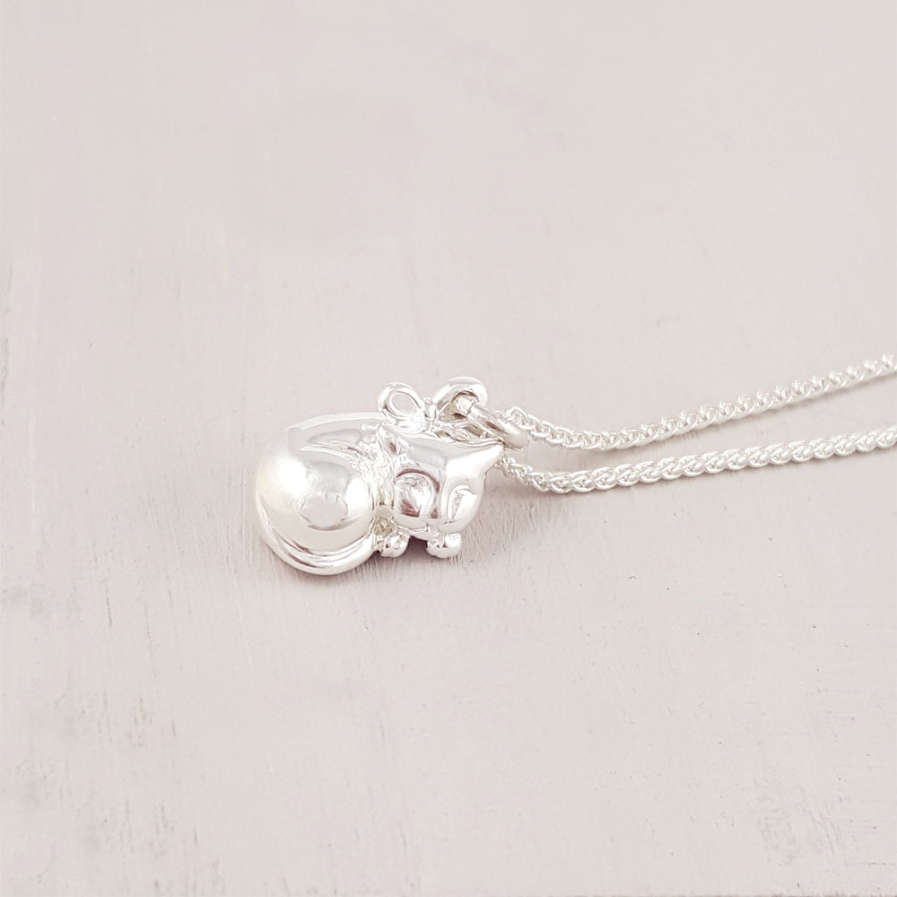 A silver cat charm with intricate detailing, displayed on a soft fabric background, by Scarlett Jewellery.