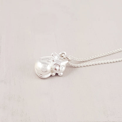 A silver cat charm with intricate detailing, displayed on a soft fabric background, by Scarlett Jewellery.