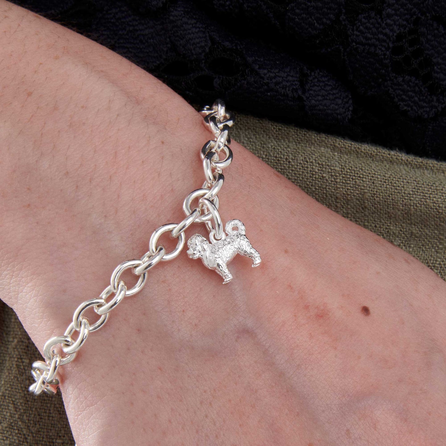 A silver cavapoo dog charm hangs on a chain, detailed and elegant, by Scarlett Jewellery.