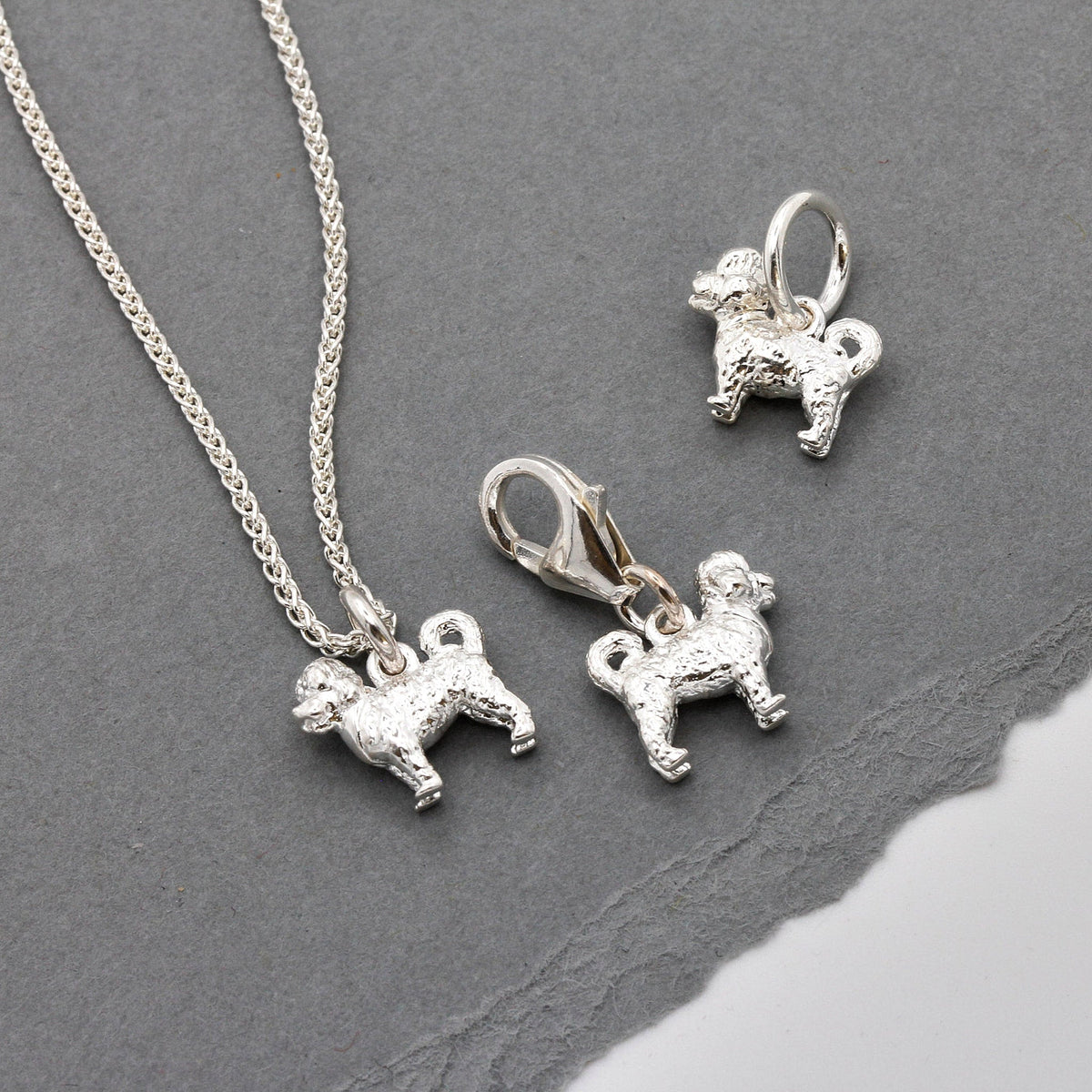A silver cavapoo dog charm shaped like a small dog, detailed with a soft texture, by Scarlett Jewellery.