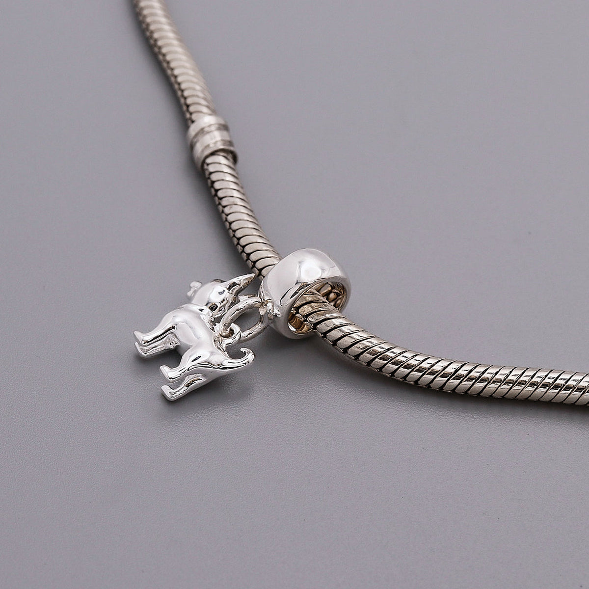 A silver chihuahua dog charm with detailed facial features, displayed on a soft pink background by Scarlett Jewellery.