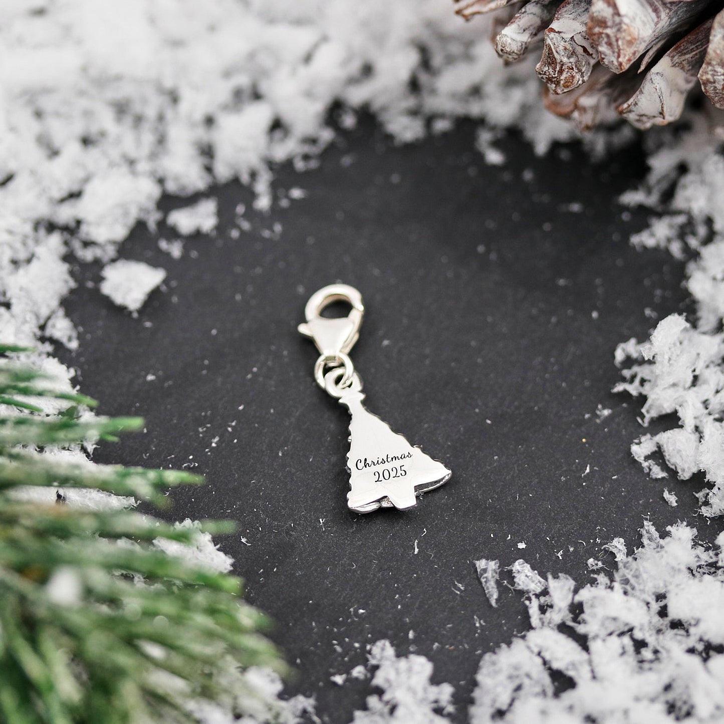 A silver Christmas tree charm with personalized engraving, displayed on a white background, by Scarlett Jewellery.