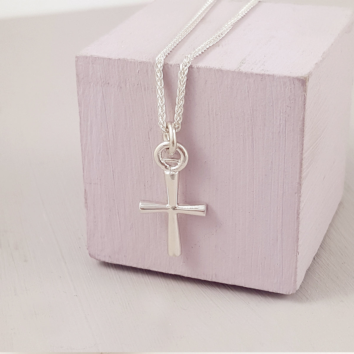 A silver cross charm glinting on a velvet background, detailed engravings visible, by Scarlett Jewellery.