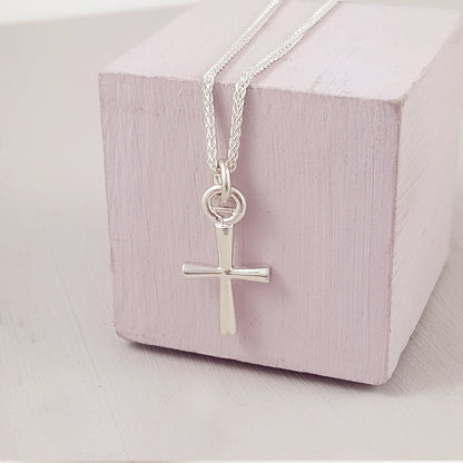 A silver cross charm glinting on a velvet background, detailed engravings visible, by Scarlett Jewellery.