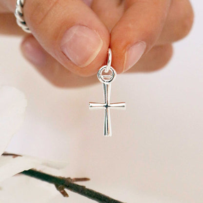 A silver cross charm glinting on a white background, detailed engravings visible, by Scarlett Jewellery.