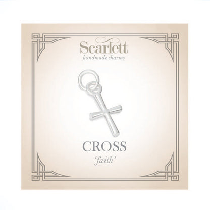 A silver cross charm glinting on a velvet background, detailed engravings visible, by Scarlett Jewellery.