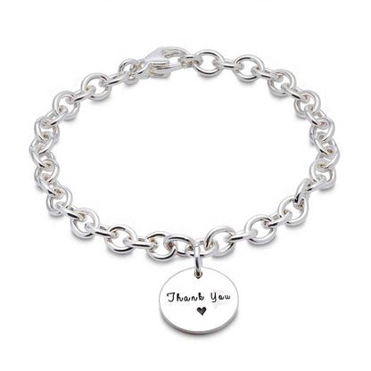 A silver round tag charm bracelet with personalized engraving, featuring a delicate chain and circular design by Scarlett Jew