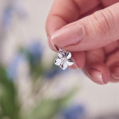 A silver forget-me-not flower charm with personalized engraving, displayed on a soft white background by Scarlett Jewellery.