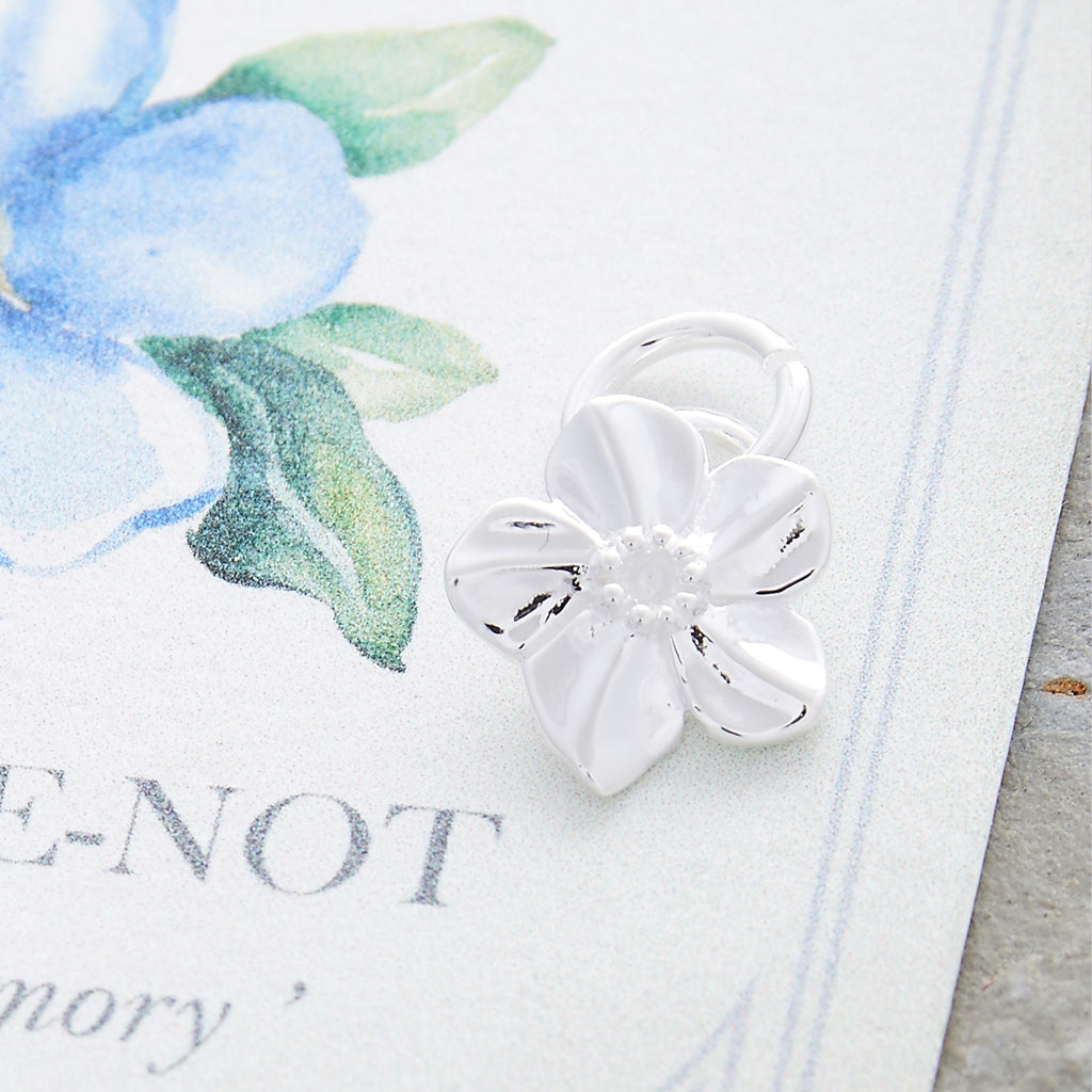 A silver forget-me-not flower charm with personalized engraving, displayed on a soft white background by Scarlett Jewellery.