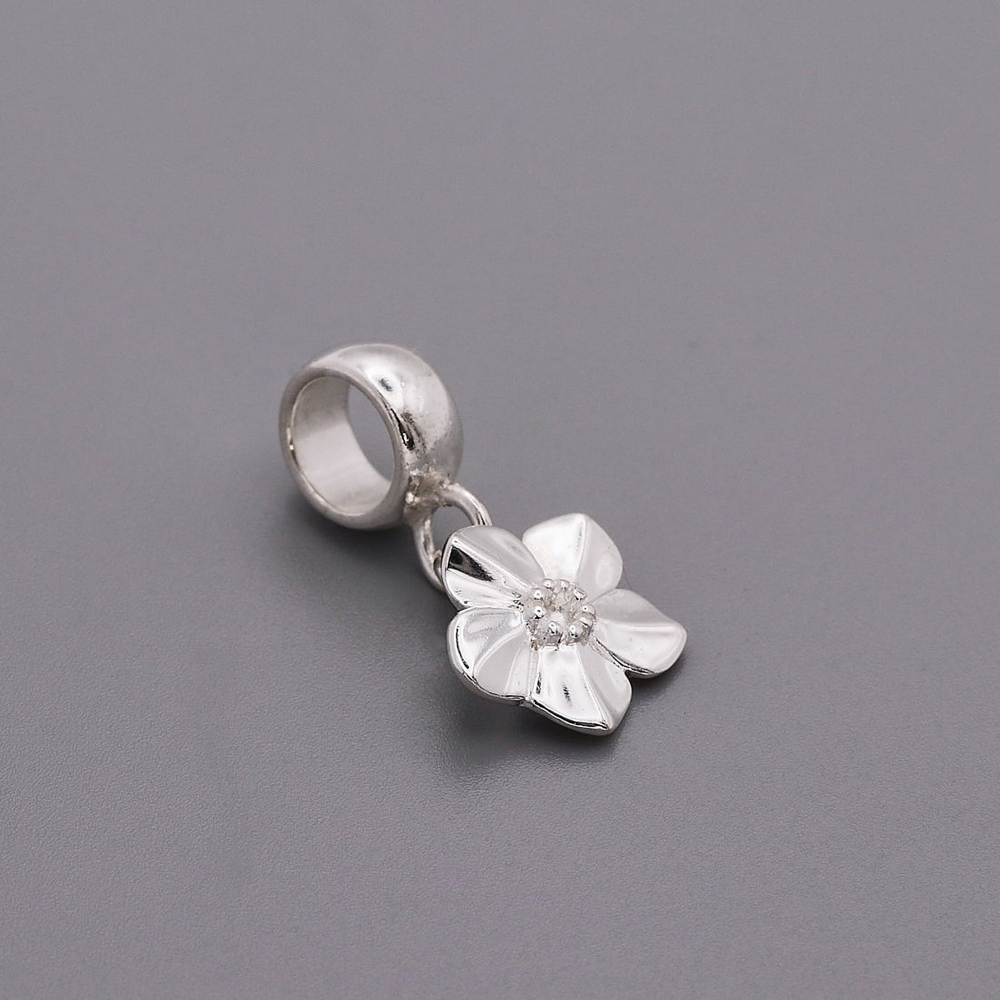 A silver forget-me-not flower charm with delicate petals, personalized engraving, and a polished finish by Scarlett Jewellery