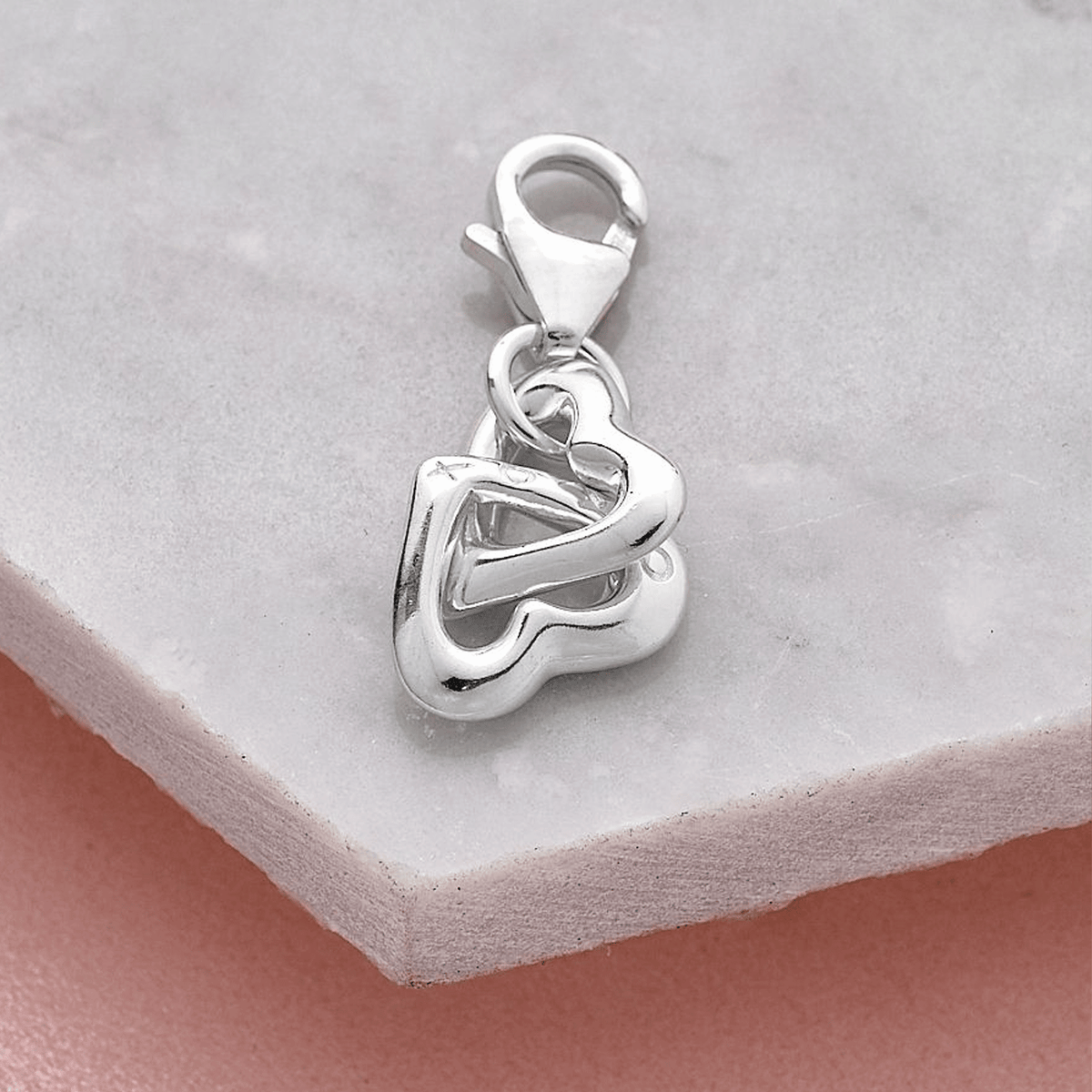 Shiny silver Friends Forever Charm featuring intertwined hearts, displayed on a marble surface by Scarlett Jewellery.