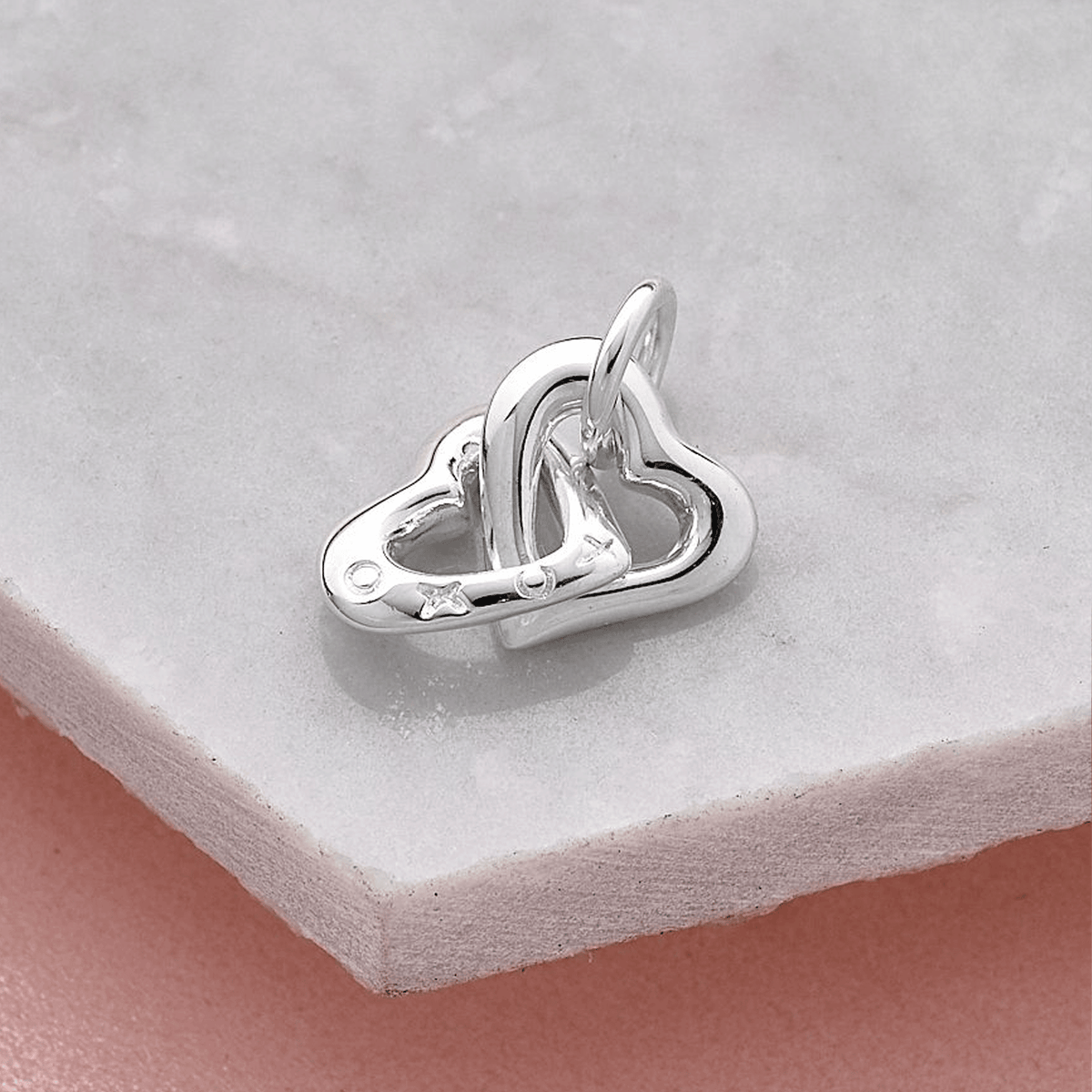Silver interlocking heart charm displayed on a smooth stone surface, showcasing the Friends Forever Charm by Scarlett Jewelle