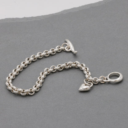 A silver heart chain charm bracelet with a detailed heart pendant, worn on the wrist by Scarlett Jewellery.