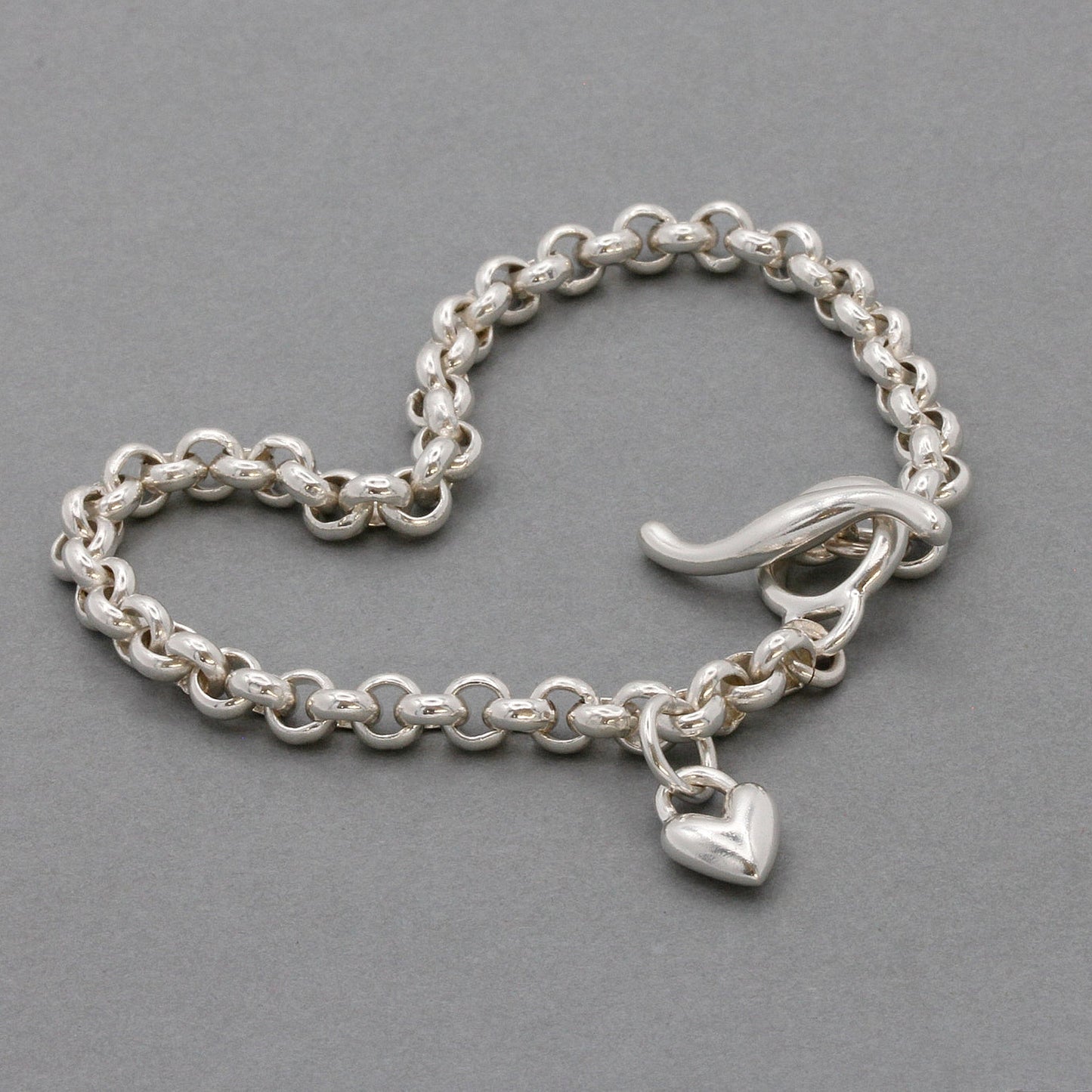 A silver heart belcher chain charm bracelet with a detailed heart charm, worn on the wrist by Scarlett Jewellery.