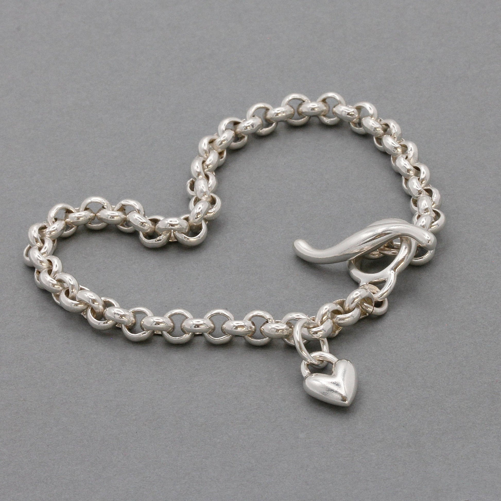 A silver heart belcher chain charm bracelet with a detailed heart charm, worn on the wrist by Scarlett Jewellery.