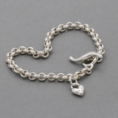 A silver heart belcher chain charm bracelet with a detailed heart charm, worn on the wrist by Scarlett Jewellery.
