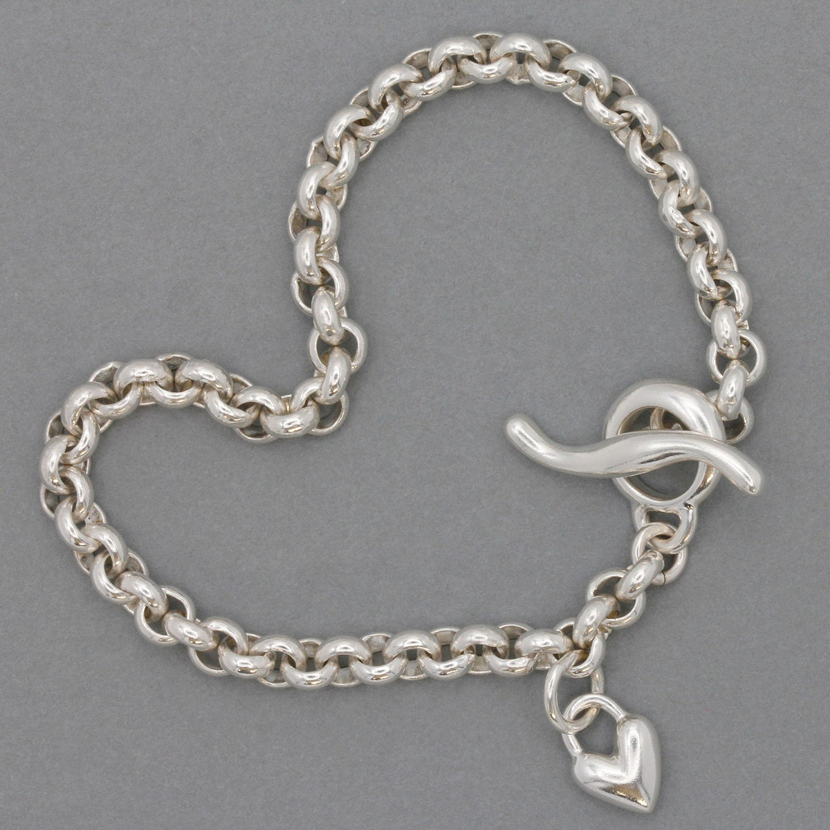 A silver heart chain charm bracelet with a detailed belcher design, featuring a central heart pendant, by Scarlett Jewellery.