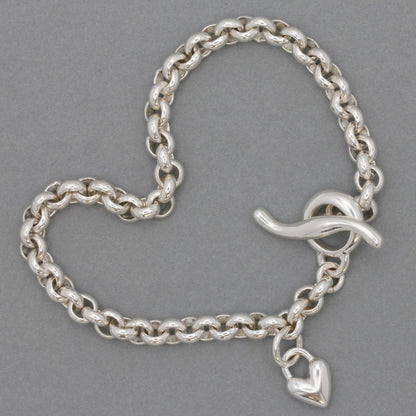 A silver heart chain charm bracelet with a detailed belcher design, featuring a central heart pendant, by Scarlett Jewellery.