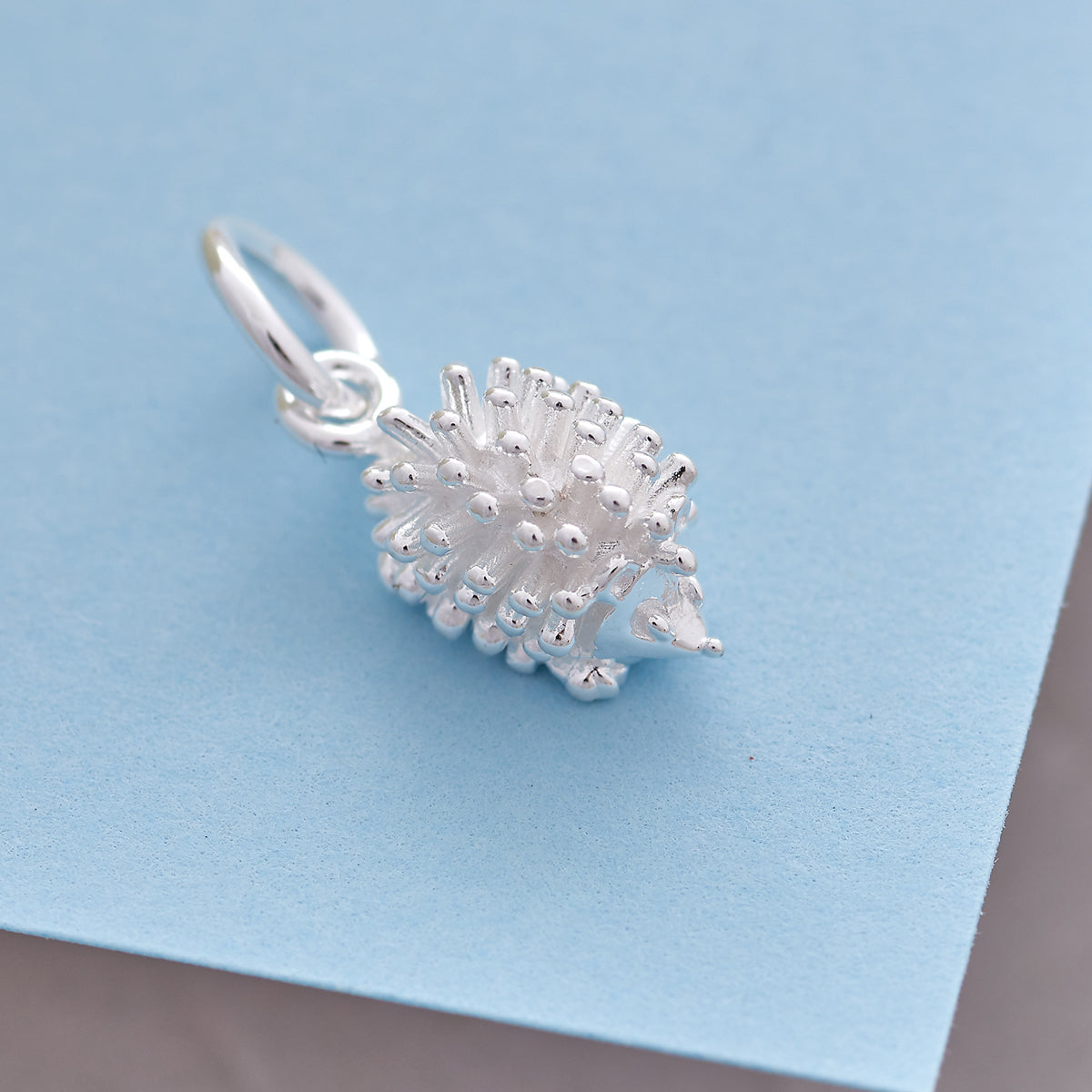 A silver hedgehog charm shaped like a small ball, detailed with texture and spikes, by Scarlett Jewellery.