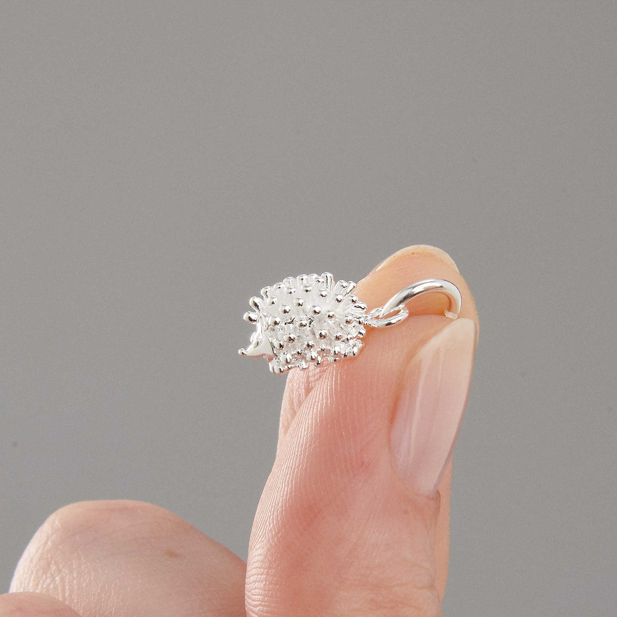 A silver hedgehog charm shaped like a small ball, detailed with texture and spikes, by Scarlett Jewellery.