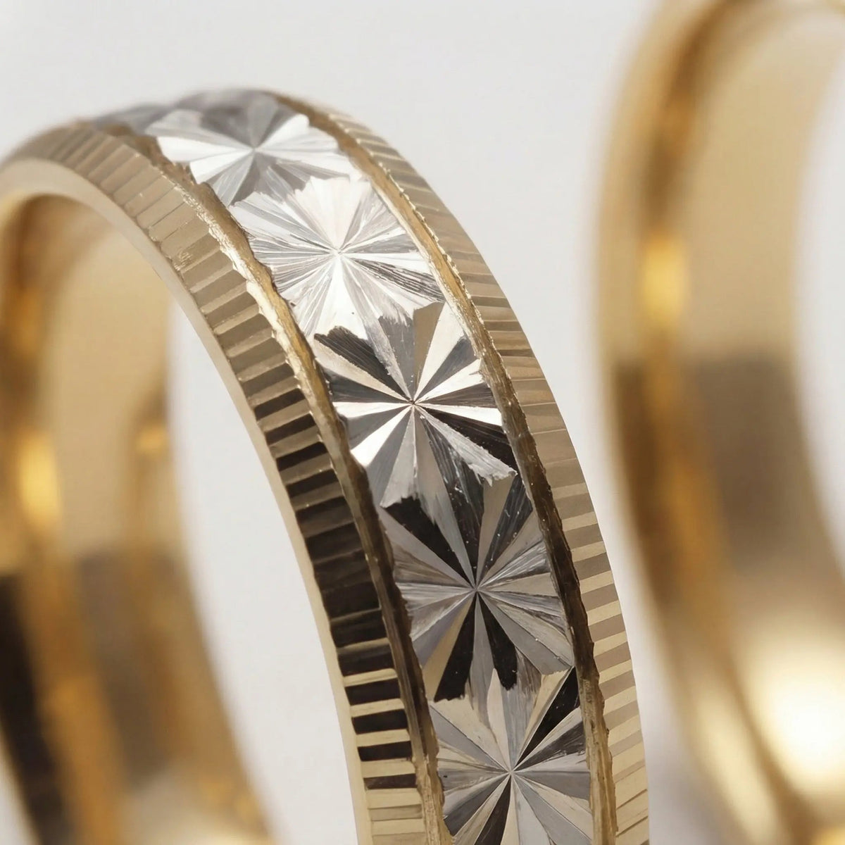A 5mm gold wedding band with a star cut design in two tone 9ct and 14ct gold worn on a finger by Majestic Jewellery