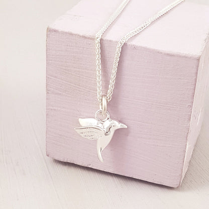 A silver hummingbird charm with detailed wings resting on a velvet background by Scarlett Jewellery.