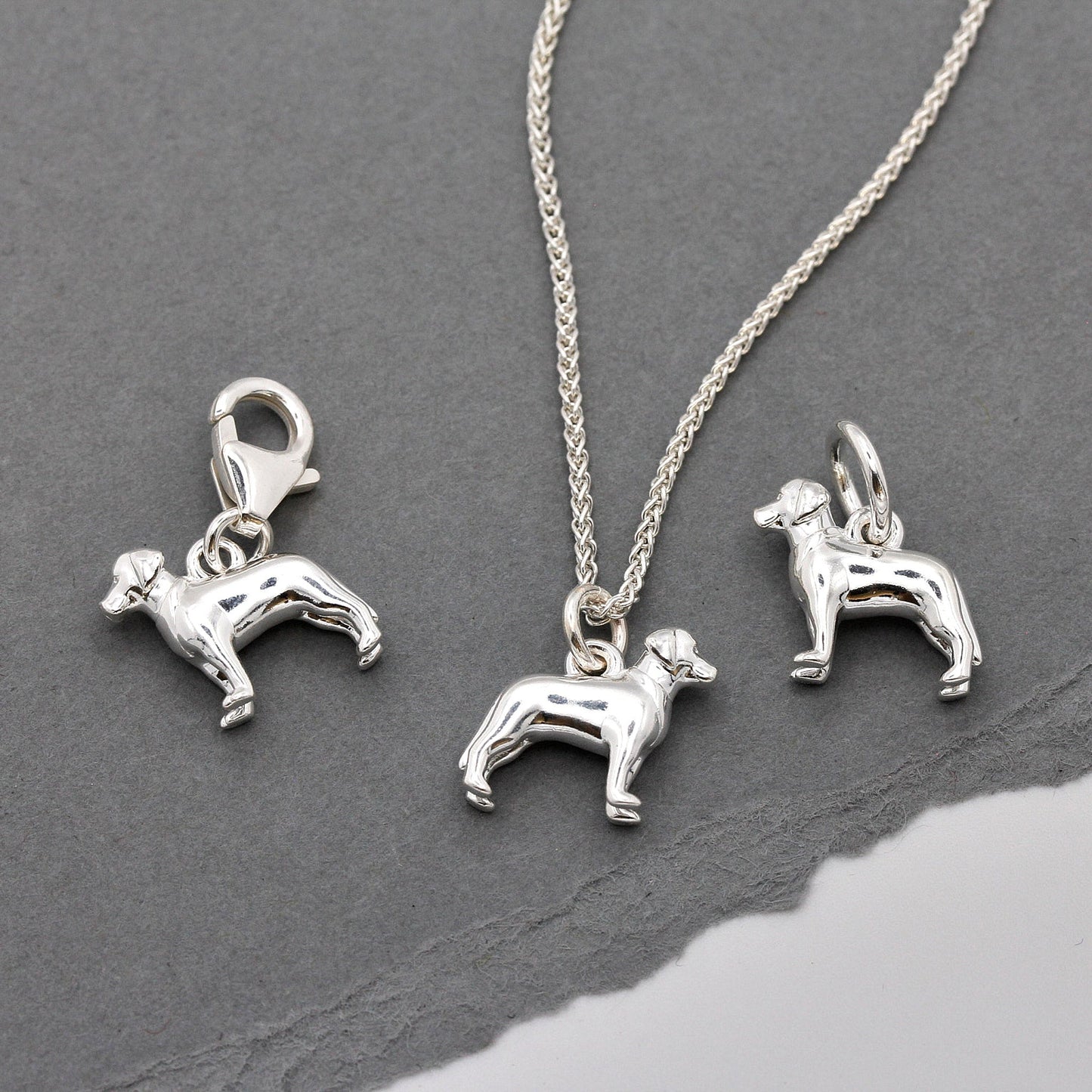 A silver Labrador dog charm shaped like a paw print, displayed on a white background with a soft texture, by Scarlett Jewelle