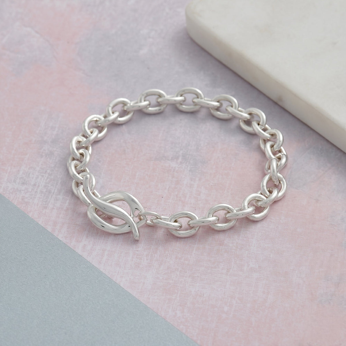 A silver charm bracelet with a heart-shaped charm, detailed engravings, and a polished finish by Scarlett Jewellery.
