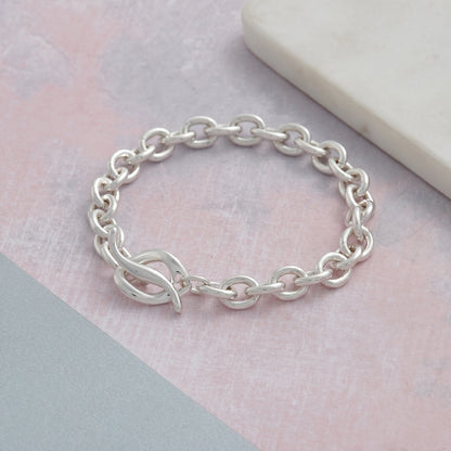 A silver charm bracelet with a heart-shaped charm, detailed engravings, and a polished finish by Scarlett Jewellery.