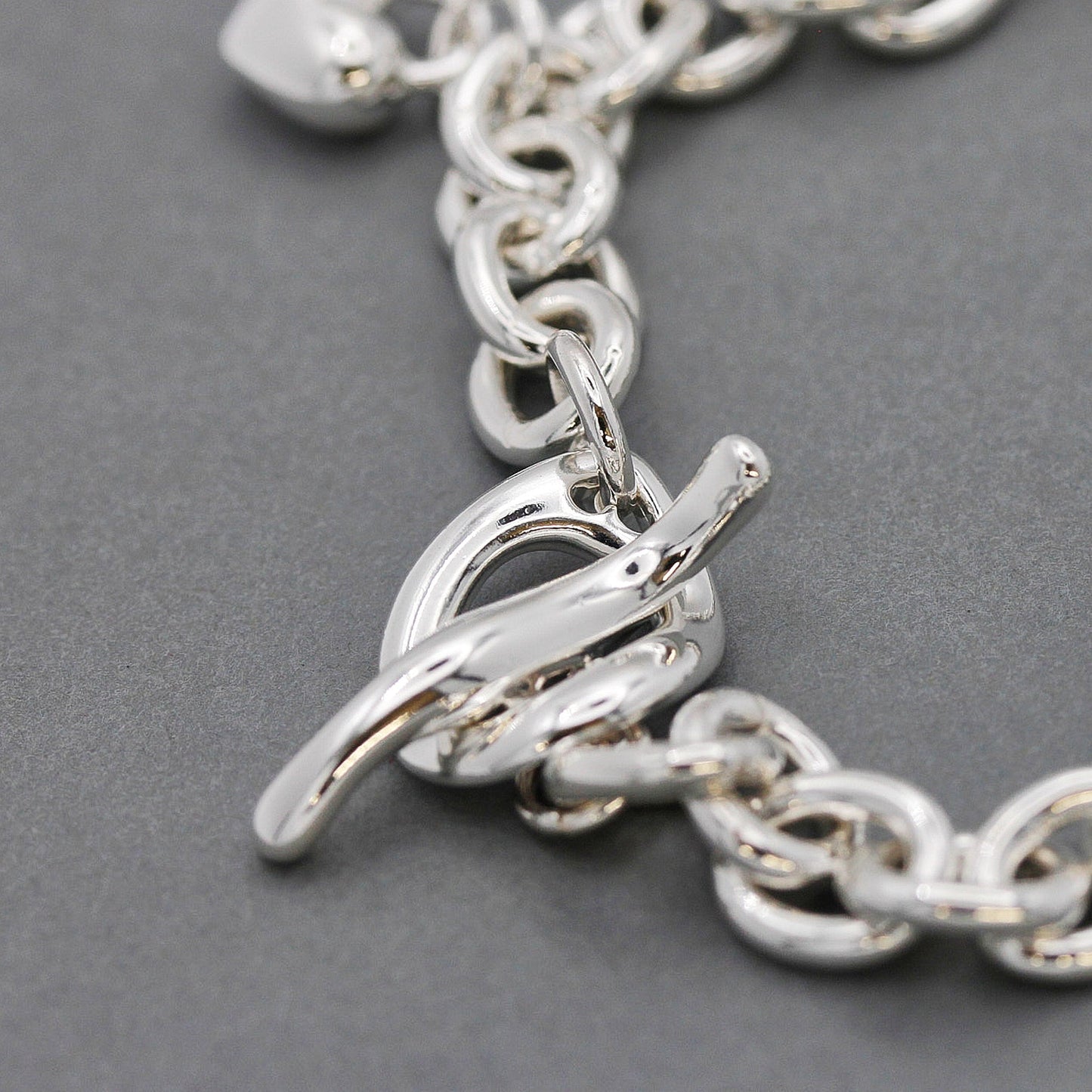 A silver heart charm bracelet with a detailed heart pendant and polished finish by Scarlett Jewellery.