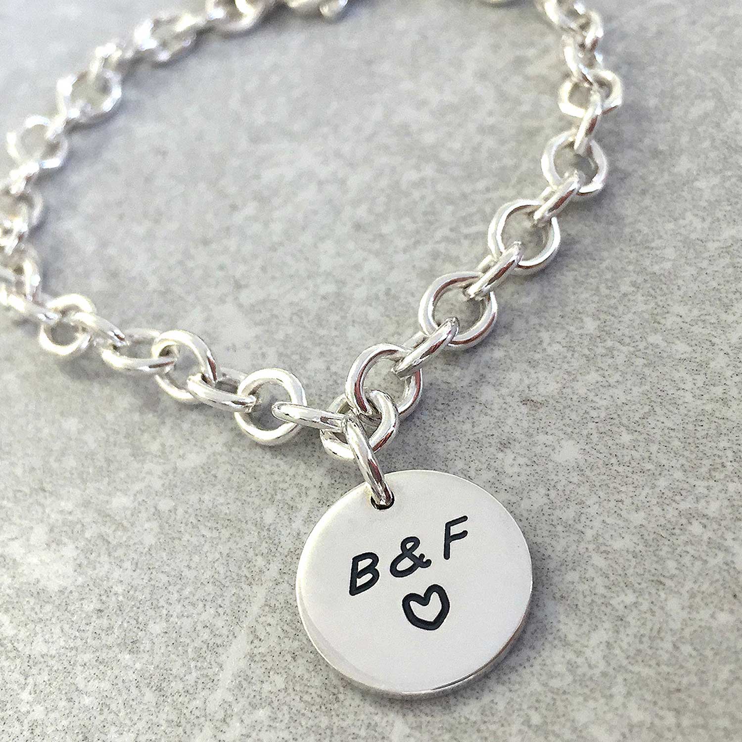 A silver round tag charm bracelet with personalized engraving, featuring a delicate chain and circular pendant, by Scarlett J