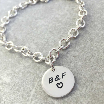 A silver round tag charm bracelet with personalized engraving, featuring a delicate chain and circular pendant, by Scarlett J