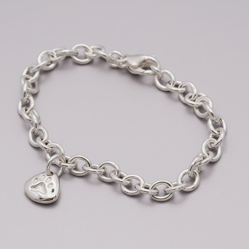 Silver paw print charm with personalized engraving, displayed on a soft blue background.