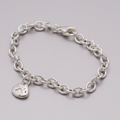 Silver paw print charm with personalized engraving, displayed on a soft blue background.
