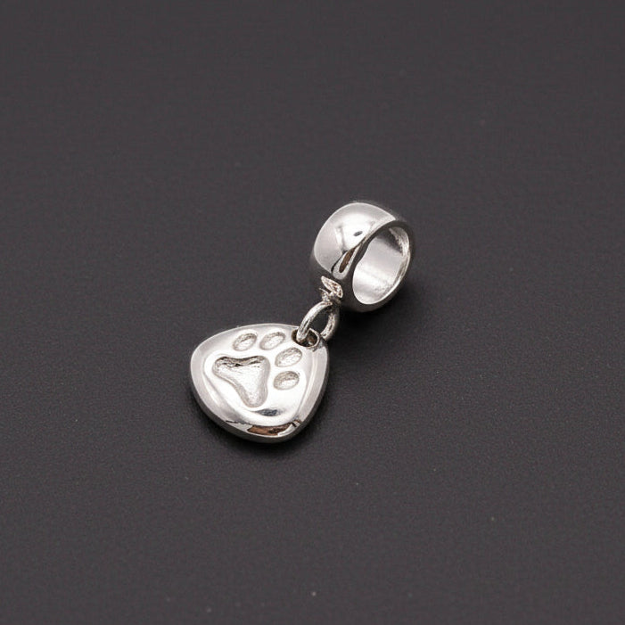 Silver paw print charm with personalized engraving, displayed on a jewelry stand by Scarlett Jewellery.