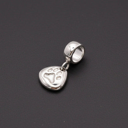 Silver paw print charm with personalized engraving, displayed on a jewelry stand by Scarlett Jewellery.