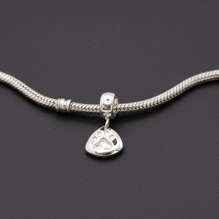 Silver paw print charm with personalized engraving, displayed on a jewelry stand by Scarlett Jewellery.