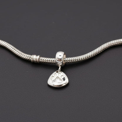 Silver paw print charm with personalized engraving, displayed on a jewelry stand by Scarlett Jewellery.