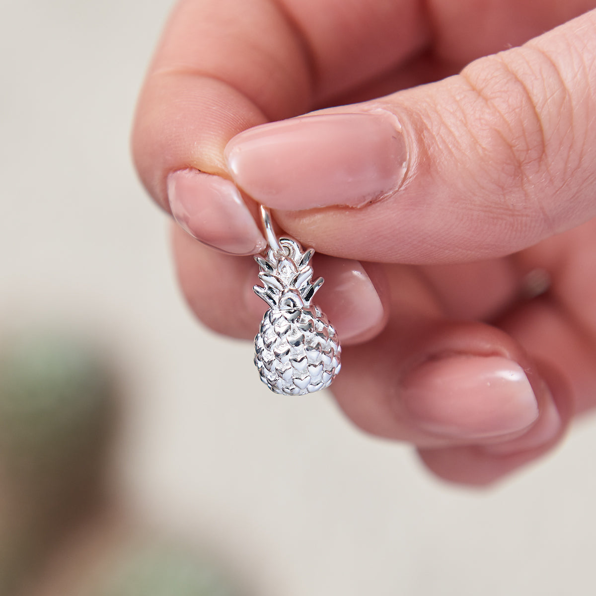 A silver pineapple charm with intricate detailing, displayed against a soft background, by Scarlett Jewellery.