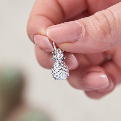 A silver pineapple charm with intricate detailing, displayed against a soft background, by Scarlett Jewellery.