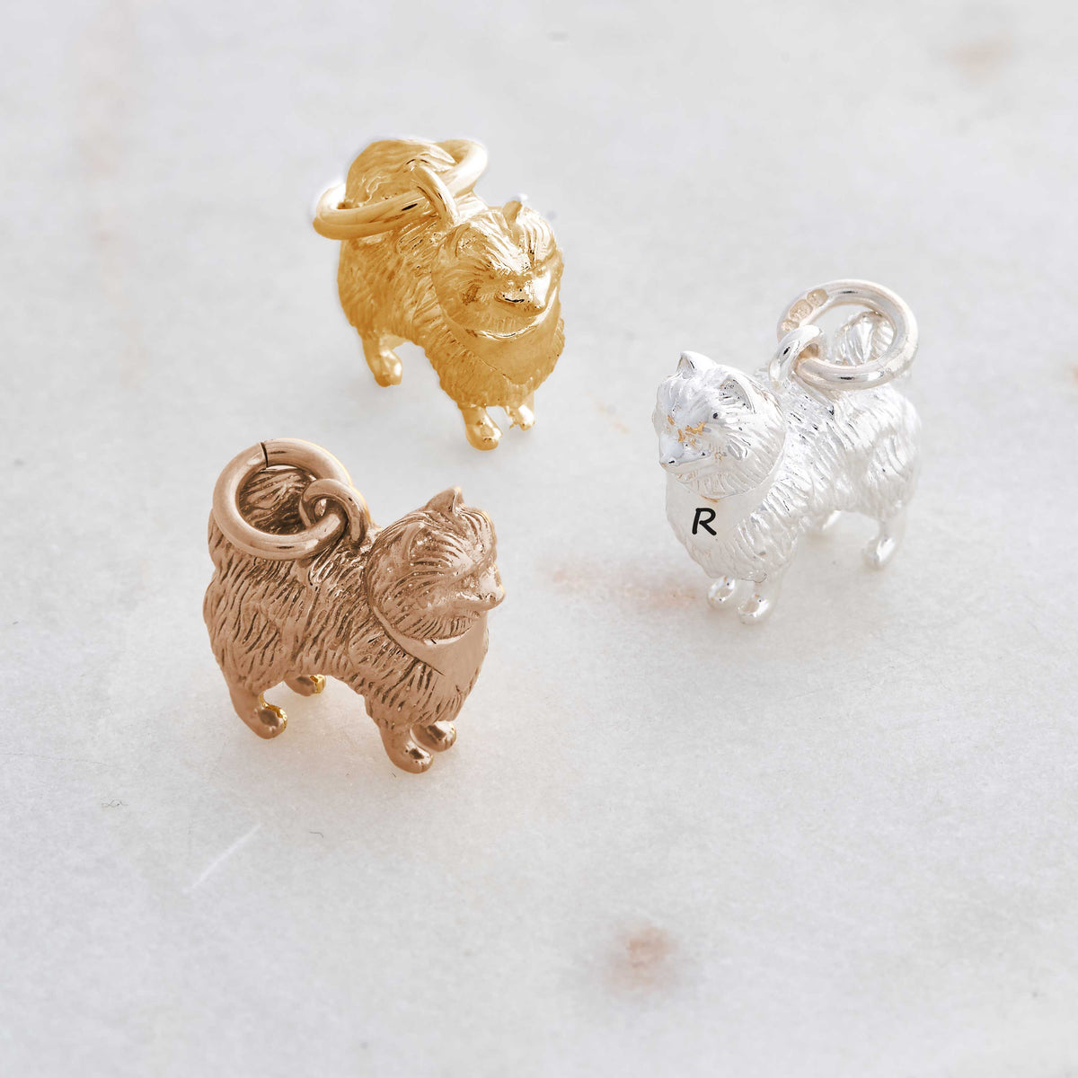 A silver Pomeranian dog charm shaped like a tiny puppy, detailed with realistic features, by Scarlett Jewellery.