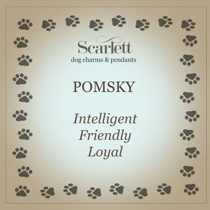 A silver pomsky dog charm with detailed facial features, displayed on a soft blue background by Scarlett Jewellery.