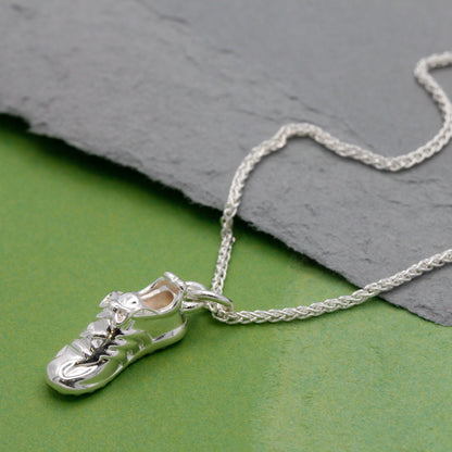 Silver running shoe charm necklace displayed on a textured background, showcasing intricate detailing. Running Shoe Silver Ch