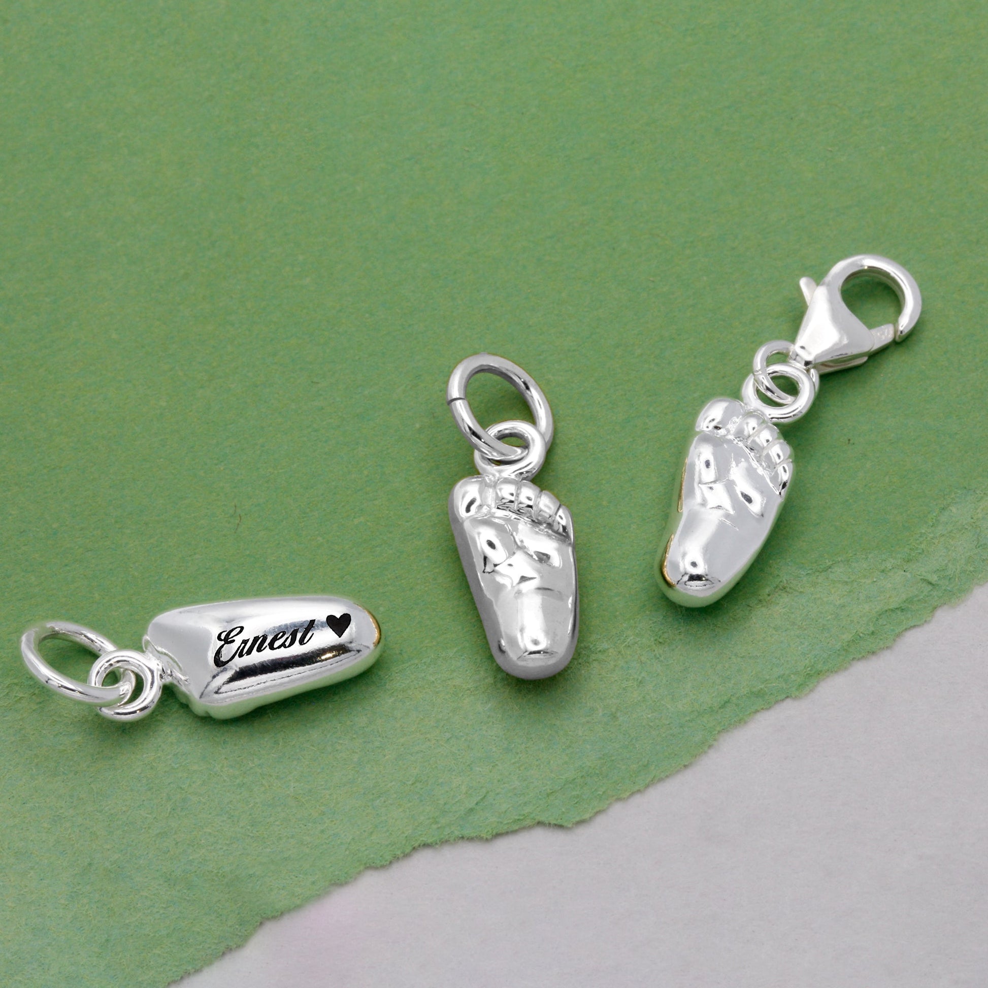 A silver baby charm with personalized engraving, displayed on a soft pink background, by Scarlett Jewellery.