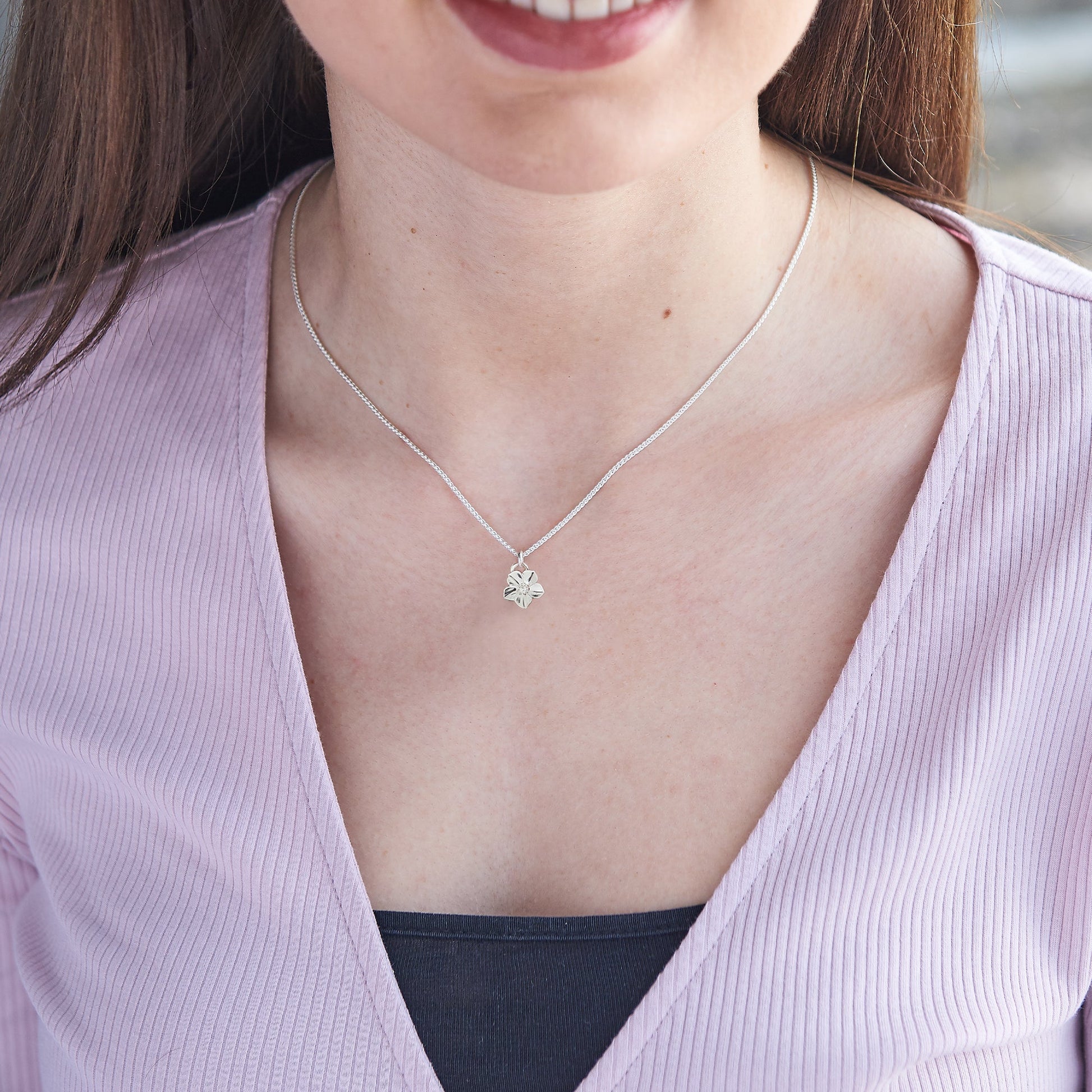Silver forget-me-not flower charm with personalized engraving, displayed on a soft background by Scarlett Jewellery.