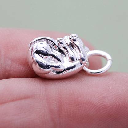 A silver cat charm with intricate detailing, displayed on a soft fabric background, by Scarlett Jewellery.