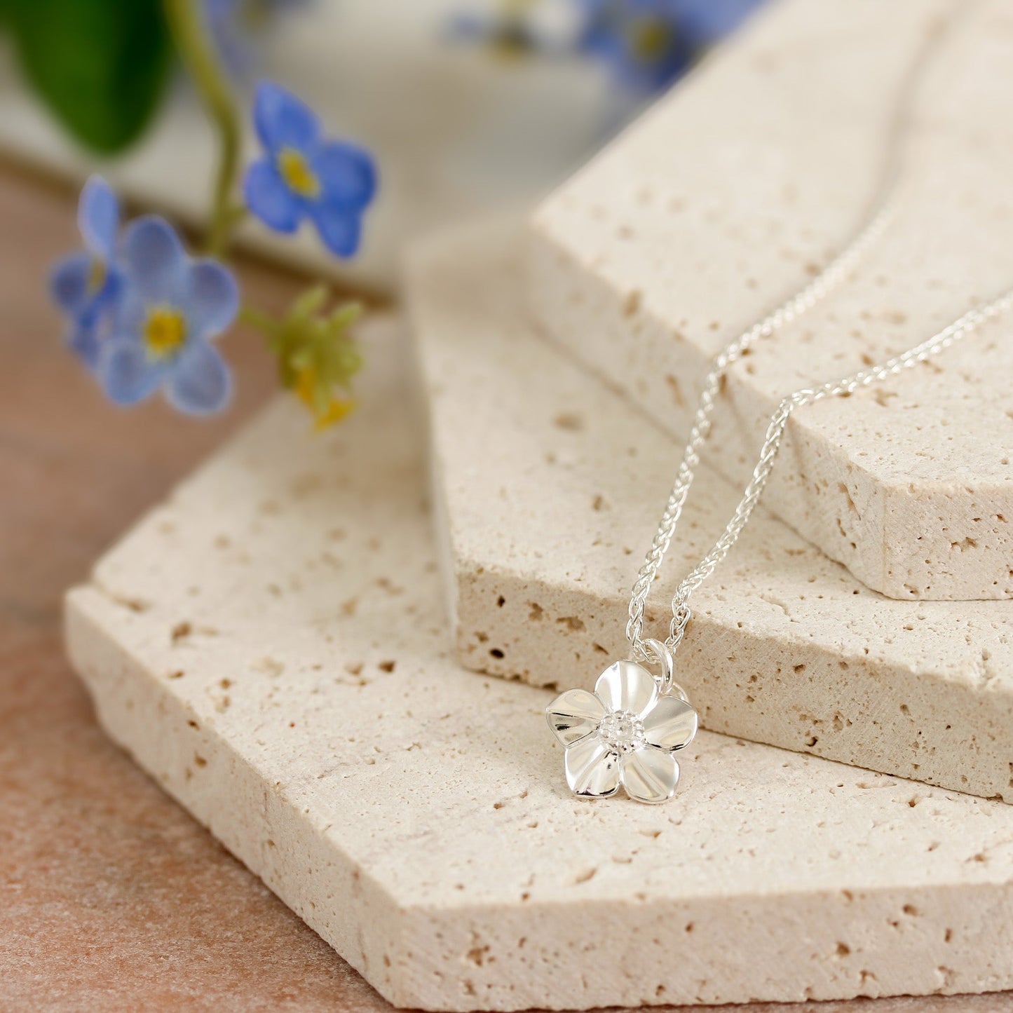Silver forget-me-not flower charm with personalized engraving, displayed on a velvet background by Scarlett Jewellery.