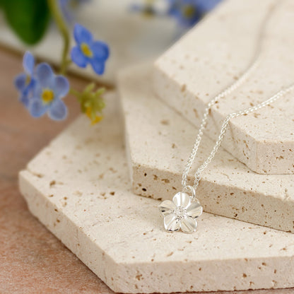 Silver forget-me-not flower charm with personalized engraving, displayed on a velvet background by Scarlett Jewellery.