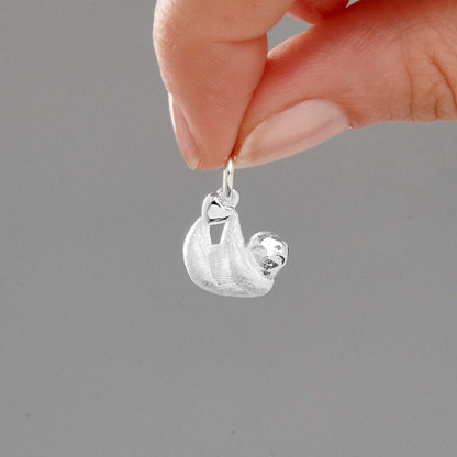 A silver sloth charm hangs from a chain, detailed and delicate, by Scarlett Jewellery.